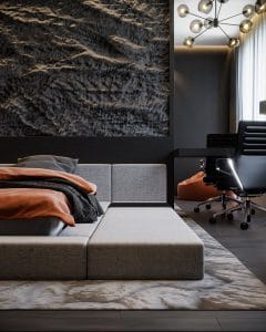 Elegant modern bedroom with textured wall art, a cozy grey bed with orange accents, stylish lighting, and an office chair, showcasing a sophisticated blend of comfort and contemporary design.